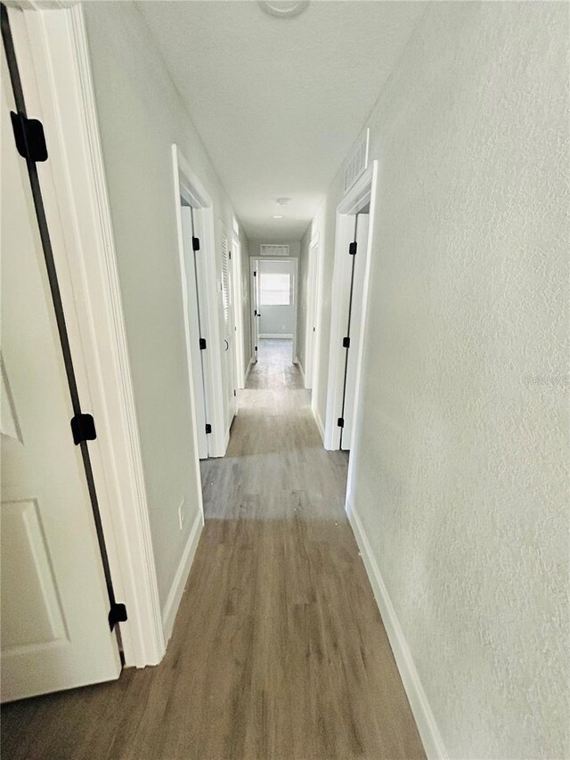 corridor with baseboards, visible vents, a textured wall, and wood finished floors