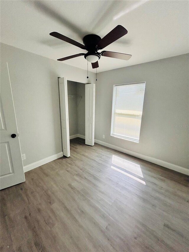 unfurnished bedroom featuring baseboards, a ceiling fan, a closet, and wood finished floors