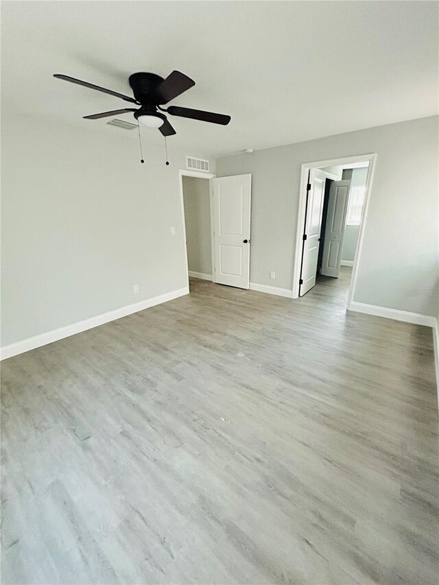 empty room with light wood-style floors, baseboards, a ceiling fan, and visible vents