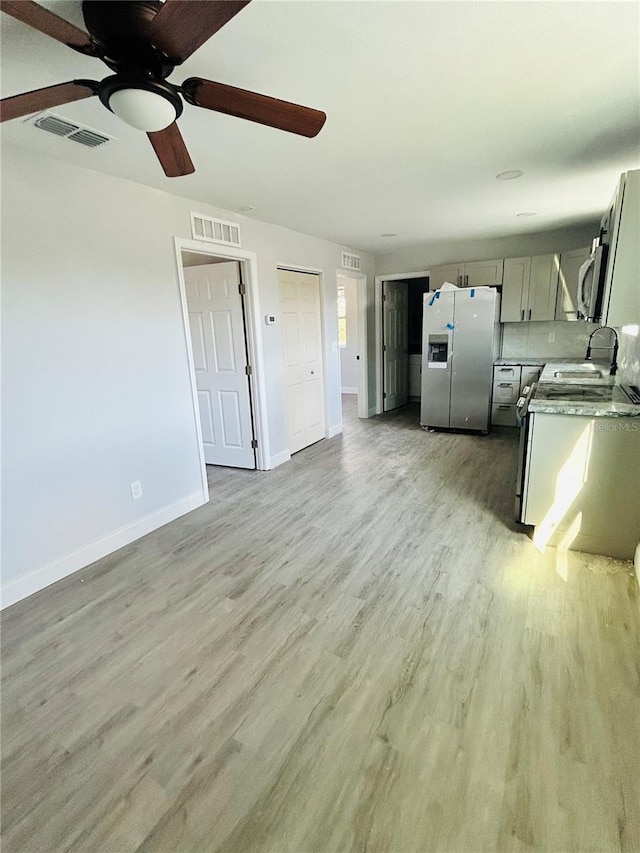 kitchen with sink, stainless steel fridge, ceiling fan, light wood-type flooring, and tasteful backsplash