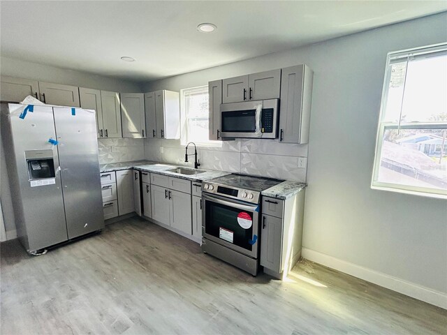 kitchen with a sink, light wood-style flooring, appliances with stainless steel finishes, and gray cabinetry