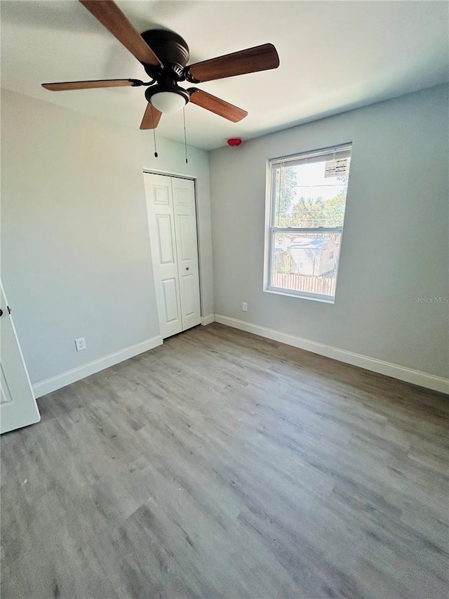 unfurnished bedroom with baseboards, ceiling fan, wood finished floors, and a closet
