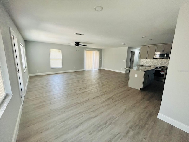 unfurnished living room featuring baseboards, ceiling fan, wood finished floors, and visible vents