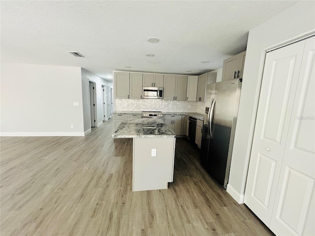 kitchen featuring visible vents, appliances with stainless steel finishes, a center island, gray cabinetry, and light stone counters