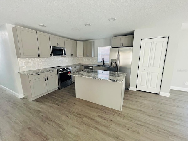 kitchen featuring appliances with stainless steel finishes, a sink, a textured ceiling, a center island, and backsplash
