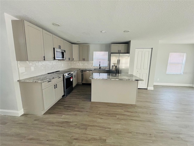 kitchen with a textured ceiling, appliances with stainless steel finishes, a sink, baseboards, and light wood-style floors