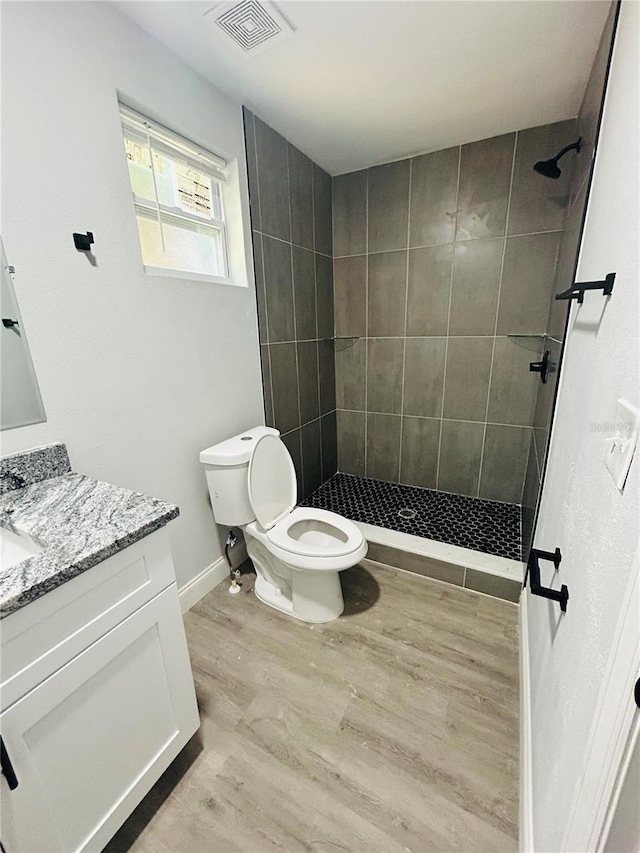 bathroom featuring vanity, toilet, wood finished floors, visible vents, and tiled shower