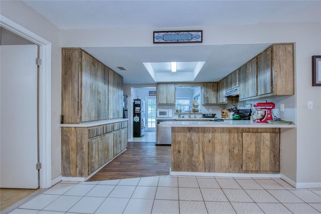 kitchen featuring sink, black range oven, white microwave, kitchen peninsula, and light hardwood / wood-style flooring