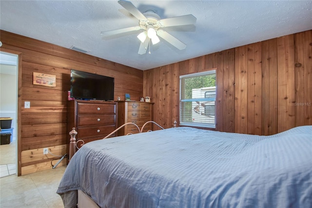 bedroom featuring a textured ceiling, wooden walls, and ceiling fan