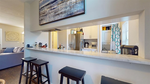 kitchen featuring stainless steel fridge with ice dispenser, white cabinetry, a kitchen bar, stacked washer / drying machine, and light stone counters