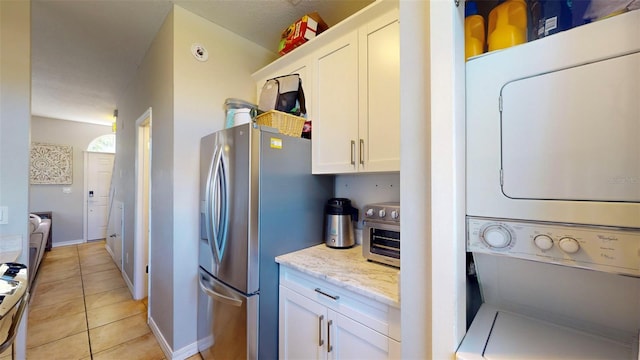 kitchen featuring light tile patterned floors, white cabinetry, light stone countertops, stacked washer / drying machine, and stainless steel refrigerator with ice dispenser