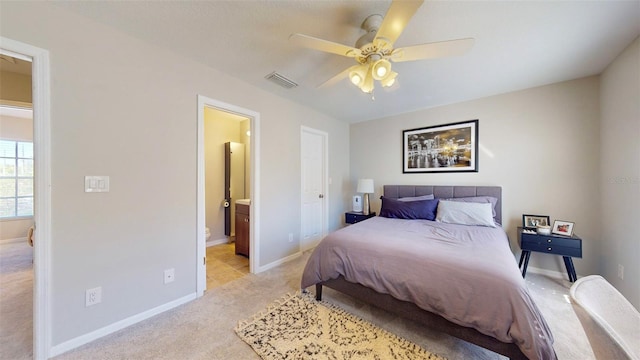 bedroom featuring ceiling fan, ensuite bathroom, and light colored carpet