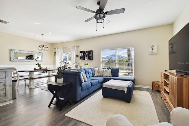 living room featuring ceiling fan with notable chandelier, a wealth of natural light, and dark wood-type flooring