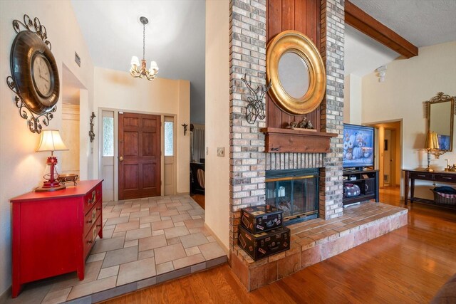 entrance foyer with high vaulted ceiling, a fireplace, light hardwood / wood-style floors, beam ceiling, and a notable chandelier