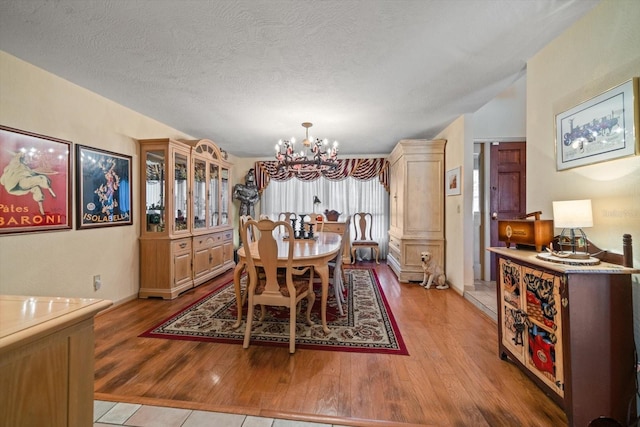 dining room with an inviting chandelier, vaulted ceiling, a textured ceiling, and light hardwood / wood-style floors