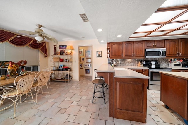 kitchen with kitchen peninsula, backsplash, sink, a breakfast bar, and appliances with stainless steel finishes