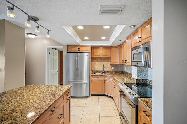 kitchen featuring backsplash, a textured ceiling, light stone countertops, a tray ceiling, and stainless steel appliances