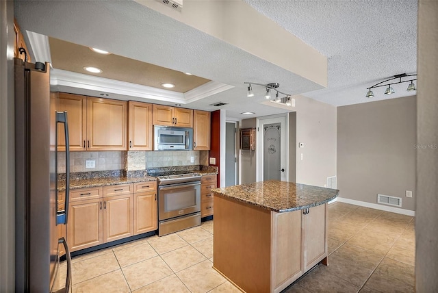 kitchen with decorative backsplash, a kitchen island, stainless steel appliances, dark stone countertops, and a textured ceiling