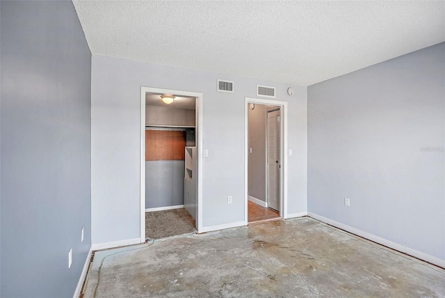 unfurnished bedroom with a closet, concrete floors, a textured ceiling, and a walk in closet