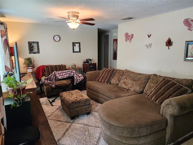 living room with ceiling fan, a textured ceiling, and light wood-type flooring