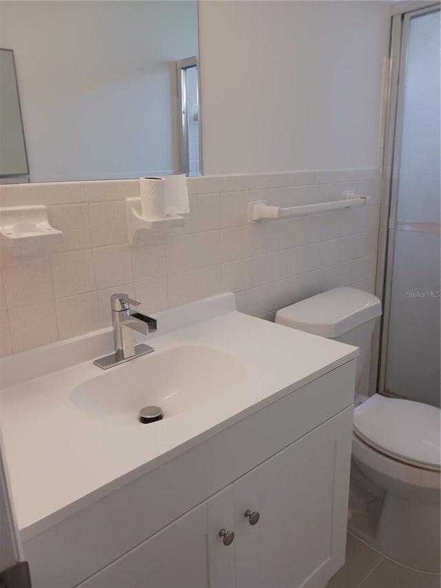 bathroom with tile walls, vanity, toilet, and tile patterned floors