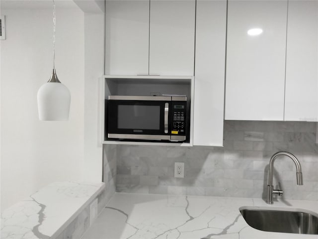 interior space featuring sink, light stone countertops, decorative backsplash, and white cabinets