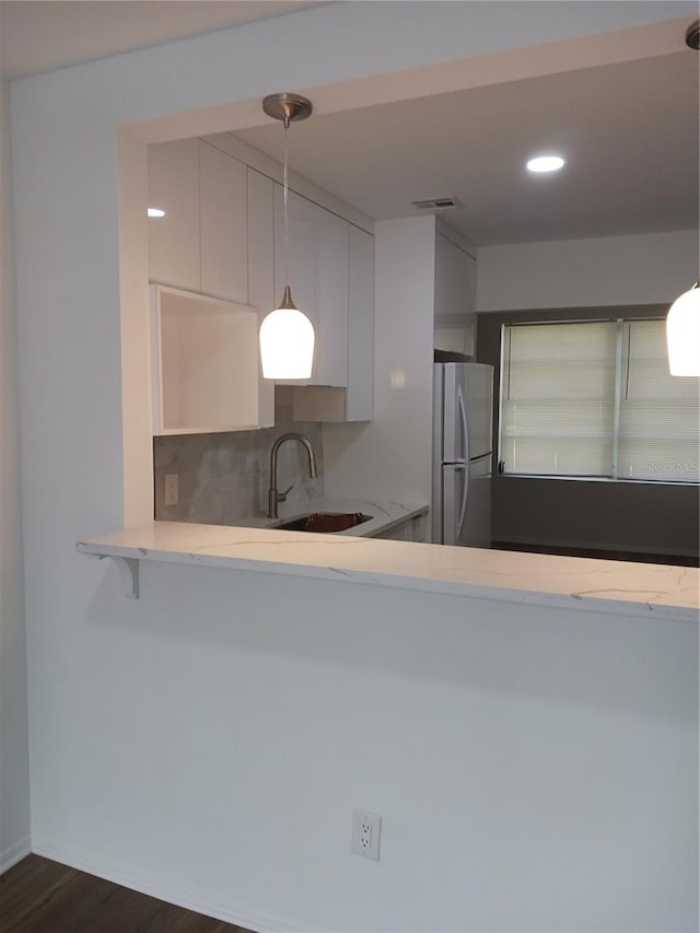 kitchen featuring dark hardwood / wood-style floors, sink, stainless steel fridge, pendant lighting, and white cabinetry