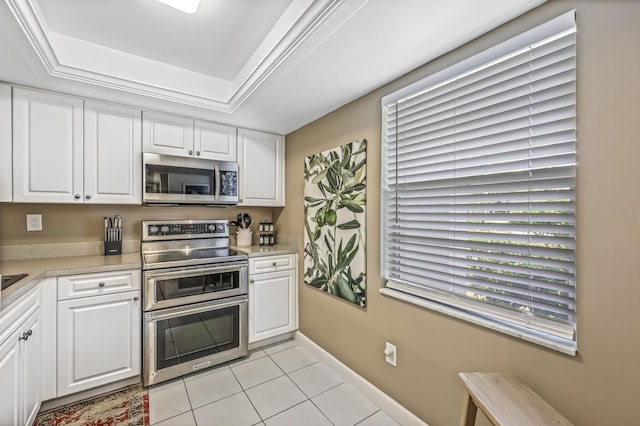 kitchen featuring white cabinetry, stainless steel appliances, a tray ceiling, and light tile patterned floors