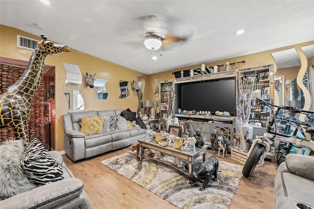 living room featuring a textured ceiling, light wood-type flooring, and ceiling fan