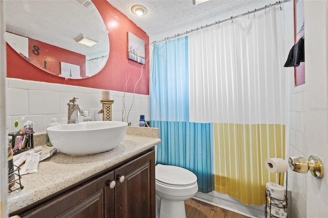 bathroom featuring a textured ceiling, wood-type flooring, tile walls, toilet, and vanity