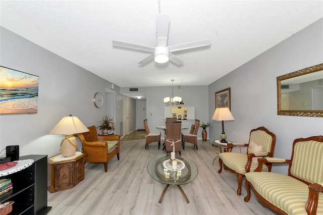 living area with ceiling fan with notable chandelier and light hardwood / wood-style floors