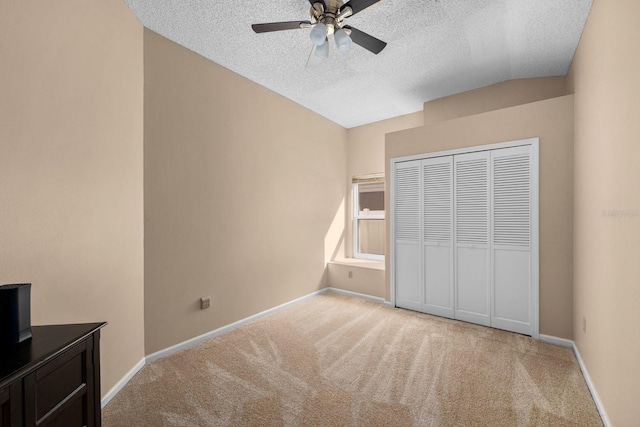 unfurnished bedroom featuring a textured ceiling, a closet, lofted ceiling, light colored carpet, and ceiling fan