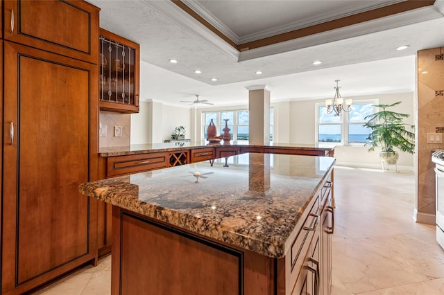 kitchen with kitchen peninsula, dark stone counters, crown molding, a center island, and ceiling fan with notable chandelier