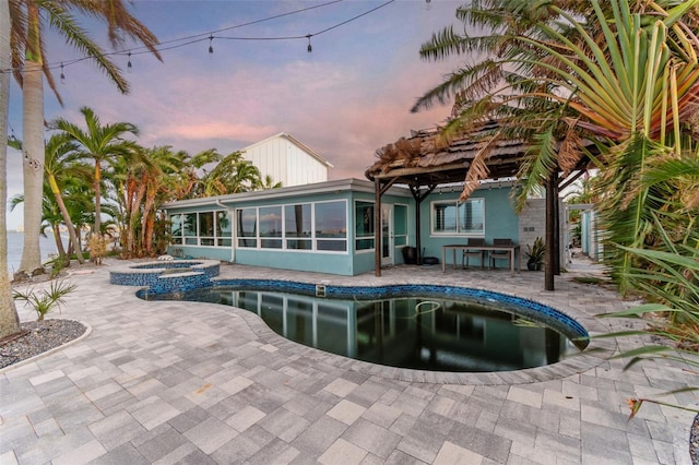 back house at dusk with a sunroom, a patio area, and a pool with hot tub