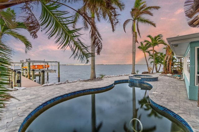 pool at dusk featuring a patio, an in ground hot tub, a water view, and a boat dock