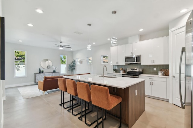 kitchen featuring white cabinets, a kitchen island with sink, sink, pendant lighting, and stainless steel appliances