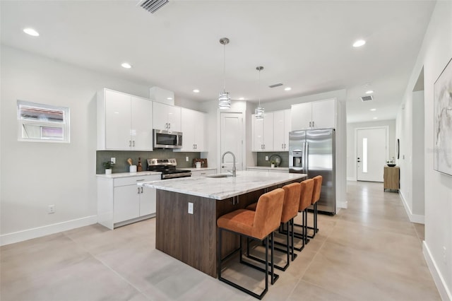 kitchen with white cabinets, tasteful backsplash, a center island with sink, appliances with stainless steel finishes, and sink