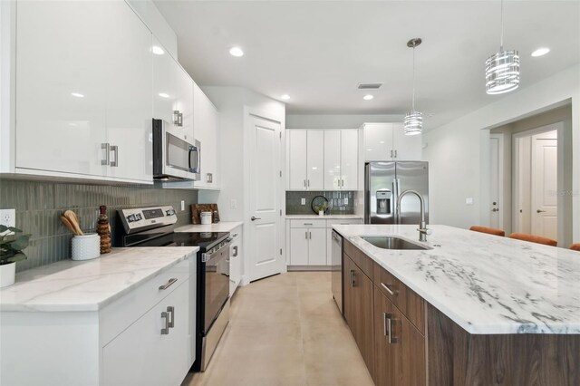 kitchen featuring tasteful backsplash, stainless steel appliances, pendant lighting, white cabinets, and a kitchen island with sink