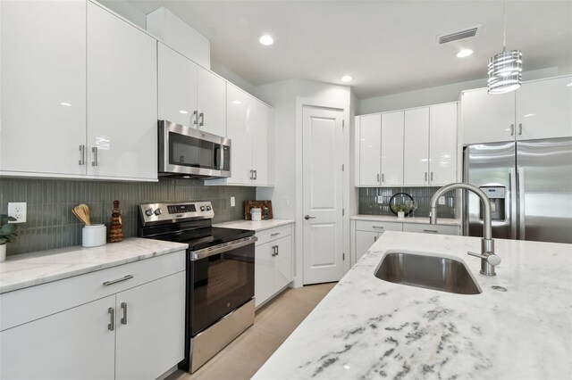 kitchen featuring decorative backsplash, hanging light fixtures, stainless steel appliances, sink, and white cabinets