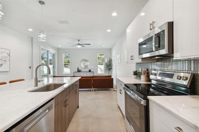 kitchen with sink, white cabinetry, stainless steel appliances, pendant lighting, and light stone counters