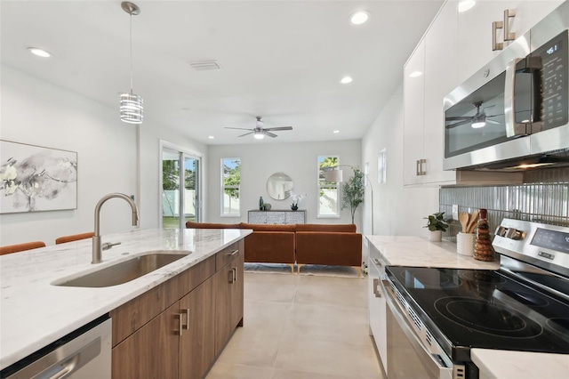 kitchen featuring hanging light fixtures, appliances with stainless steel finishes, white cabinetry, light stone countertops, and sink