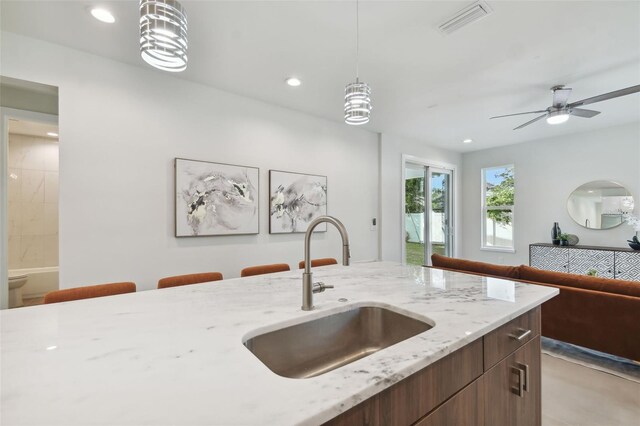 kitchen featuring light stone counters, sink, pendant lighting, and ceiling fan