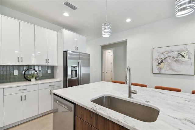 kitchen featuring hanging light fixtures, stainless steel appliances, sink, white cabinets, and tasteful backsplash