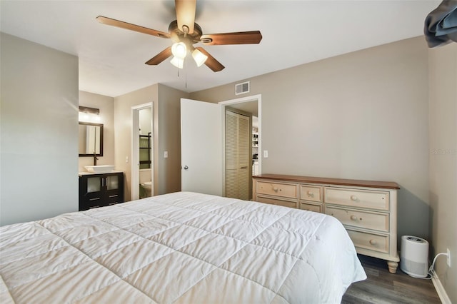 bedroom with dark wood-type flooring, ensuite bathroom, a closet, and ceiling fan