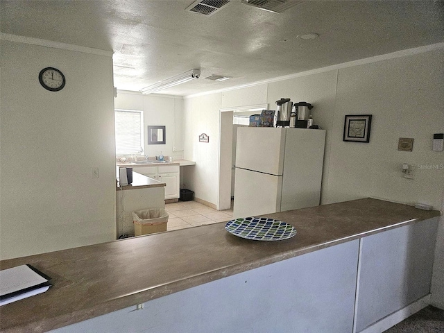 kitchen with white fridge, light tile patterned floors, ornamental molding, and white cabinetry