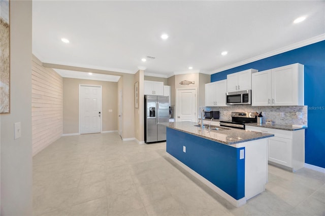 kitchen with an island with sink, appliances with stainless steel finishes, white cabinetry, dark stone counters, and sink