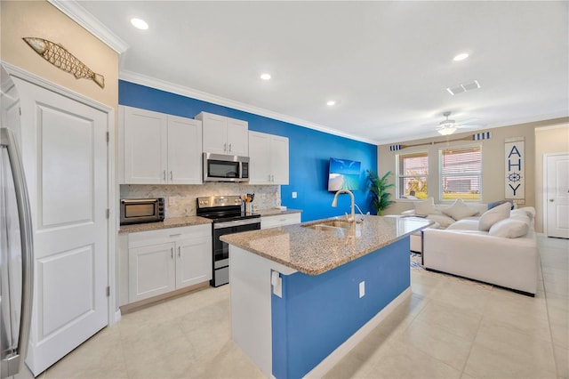 kitchen featuring a kitchen island with sink, stainless steel appliances, sink, light stone countertops, and white cabinetry