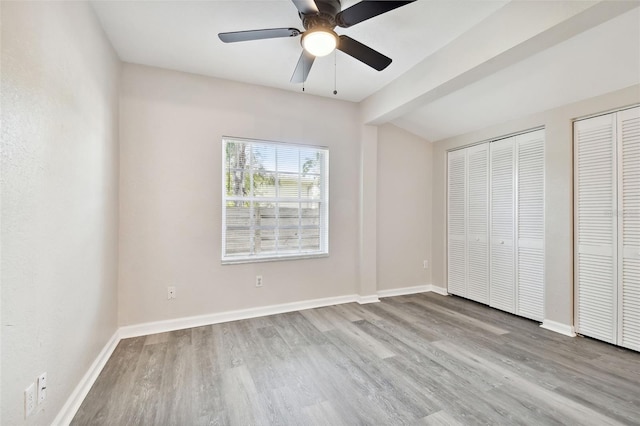 unfurnished bedroom featuring multiple closets, light wood-type flooring, and ceiling fan