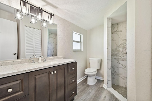 bathroom with a tile shower, a textured ceiling, hardwood / wood-style flooring, toilet, and vanity