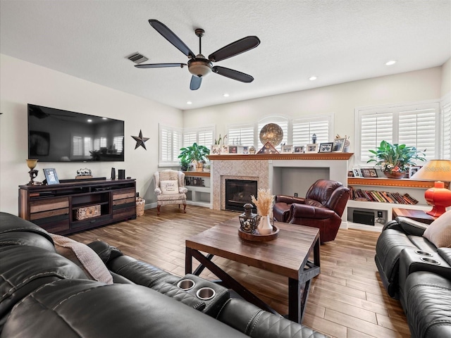 living room with a healthy amount of sunlight, a tiled fireplace, and wood-type flooring